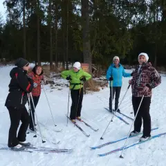 Grupa osób w strojach na narty biegowe pozuje do zdjęcia w lesie.