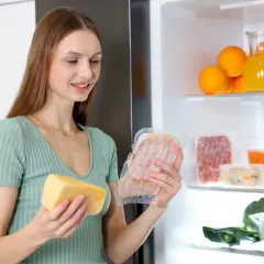 Kobieta wybiera wędlinę z lodówki, uważając na potencjalną obecność listerii. Obok ser i inne produkty.