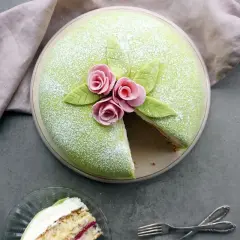 En vacker prinsesstårta med grönt marsipanlock, rosa rosor och blad. Ett stycke är uppskuret, perfekt för att inspireras av ett prinsesstårta recept.