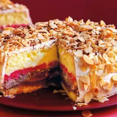 Una fetta di pizza dolce abruzzese, con strati di crema, cioccolato e confettura, ricoperta di mandorle tostate e panna.