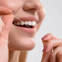 Primo piano di una donna che usa il filo interdentale per pulire i denti. Impara scovolino denti come si usa per un sorriso smagliante.