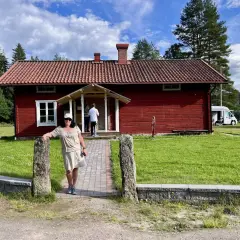 Värnäs camping: En kvinna står vid en röd stuga med tegeltak. Husbilar syns i bakgrunden under en blå himmel med moln.
