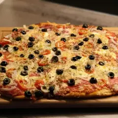 Frisch gebackene Pizza mit Tomaten, Oliven und Käse auf einem Holzbrett. Der Pizzateig wurde im Thermomix zubereitet.