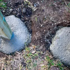 Zwei Holzpfosten werden gerade in frisch gegossenen Beton gesetzt, um sie sicher zu verankern. Das Einbetonieren von Zaunpfosten sorgt für Stabilität.