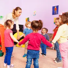 Nauczycielka z dziećmi w przedszkolu trzymają się za ręce. Czy można przenieść dziecko do innej grupy bez zgody rodziców?