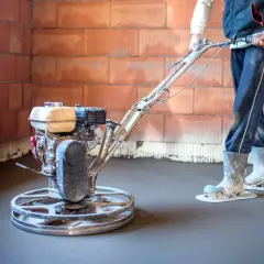 Operaio usa una levigatrice per cemento per lisciare il pavimento di una casa in costruzione.