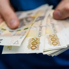 Dłonie trzymają plik banknotów 200 zł. Zastanawiasz się, ile wynosi zasiłek dla bezrobotnych?