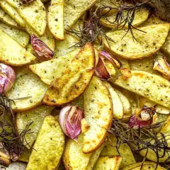 Patatas rústicas asadas con ajo y romero, doradas y crujientes en una bandeja.