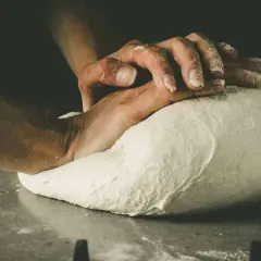 Hände kneten den Pizzateig. Die Frage "wie lange pizzateig kneten" beschäftigt jeden Bäcker.
