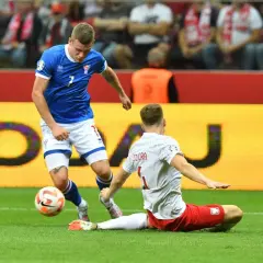 Piłkarz w niebieskiej koszulce walczy o piłkę z zawodnikiem w białej, próbującym go zatrzymać. Mecz Polska - Wyspy Owcze.