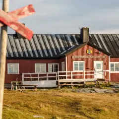 STF Blåhammaren Fjällstation, en röd fjällstuga med vita detaljer, välkomnar vandrare i ett kargt landskap.