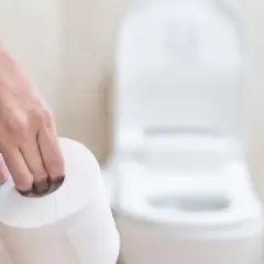 Dłoń trzymająca rolkę papieru toaletowego przed toaletą. Może to sugerować problemy z wypróżnianiem, co powoduje zaparcia.