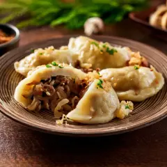 Pyszne pierogi z kapustą i grzybami, posypane szczypiorkiem, na talerzu z widelcem obok.