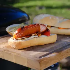 Pyszna kiełbasa z grilla w bułce z warzywami, gotowa do podania na desce.