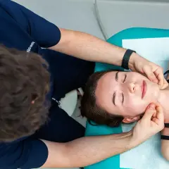 Fizjoterapeuta wykonuje masaż twarzy, co jest częścią rehabilitacji stomatologicznej.