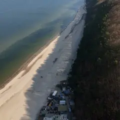 Plaża i las nad Bałtykiem. Połczyn-Zdrój odległość od morza jest niewielka, widać kilka domków i spacerowiczów.