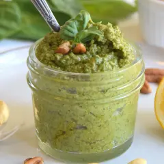 Frisches grünes Pesto in einem Glas, garniert mit Basilikum und Nüssen, daneben Knoblauch und Zitrone.