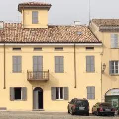 Edificio giallo con intonachino silossanico, tegole rosse, persiane grigie e balcone. Auto parcheggiate davanti.