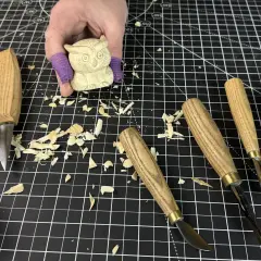 Une main tient une petite chouette en bois sculpté, entourée d'outils et de copeaux. Idéal pour une **débutant sculpture bois facile**.