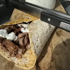 Pyszny kebab kryspinów z jakim sosem, gotowy do podania. Mięso soczyste, zawinięte w tortillę, polane białym sosem.