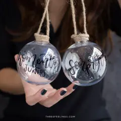Dos bolas de navidad personalizadas con nombre, una dice "hogar" y la otra "juntos".