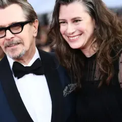 Gary Oldman z żoną, oboje uśmiechnięci, on w eleganckim garniturze, ona w czarnej sukni z koronkowymi rękawami.