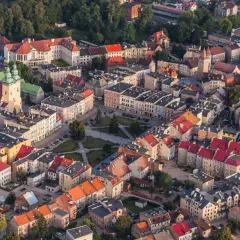 Widok z lotu ptaka na miasto z czerwonymi dachami, kościołem i placem. Może to być początek szlaku czarownic.