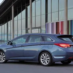 Niebieski Hyundai i40 kombi zaparkowany przed nowoczesnym budynkiem z kolorowymi pasami. Wiele osób chwali ten model, czytając **hyundai i40 opinie**.