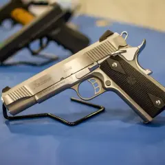 Srebrny pistolet gazowy Regent R200S na czarnym stojaku. W tle widać inne bronie.