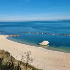 Spiaggia dorata e mare cristallino sulla Riviera del Conero, con scogliere bianche e un grande masso solitario nell'acqua.