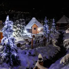 Zimowa sceneria, oświetlone choinki i przytulne chatki. Idealne miejsce, gdzie spędzić święta bożego narodzenia w magicznej atmosferze.