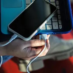 Dłoń podłącza kabel USB telefonu do laptopa, pokazując, jak połączyć telefon z laptopem.