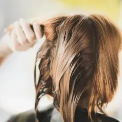 Dłoń czesze mokre, brązowe włosy, dążąc do idealnej równowagi pH dla zdrowego blasku.