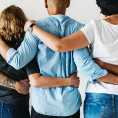 Pięć osób obejmuje się, tworząc wspierającą grupę. Ich ramiona splecione są w geście bliskości, symbolizującym związek poliamoryczny i wzajemne zaufanie.