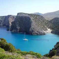 Baia con acque cristalline e una barca a vela. Le scogliere rocciose e la vegetazione mediterranea creano uno scenario suggestivo, perfetto per capire come si misura la profondità del mare.