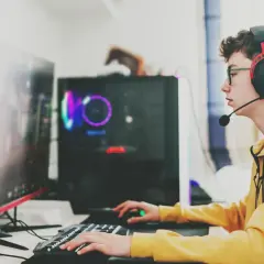 Ein junger Mann mit Kopfhörern und Brille spielt konzentriert am Computer. Sein **Computer sucht** nach neuen Herausforderungen, während er mit Tastatur und Maus agiert.