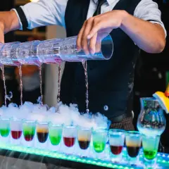 Samoobsługowy drink bar na weselu: barman nalewa kolorowe shoty z wielokomorowego shakera, tworząc efektowny pokaz.