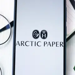 Na ekranie telefonu widnieje logo Arctic Paper. Obok leżą okulary i zielony zakreślacz, sugerując analizę akcji.