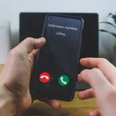 Dłoń trzyma smartfon z ekranem pokazującym "Unknown number calling..." oraz przyciski odbierania i odrzucania połączenia.