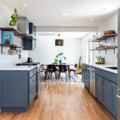 A modern kitchen with deep blue cabinets, white subway tile backsplash, and warm wood floors. The cabinet colors offer a stylish contrast to the stainless steel appliances.