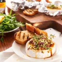 Pyszny camembert z grilla, polany miodem i posypany pistacjami, podany z grzankami i sałatką.