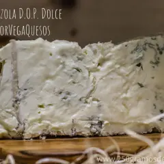 Un trozo de gorgonzola D.O.P. Dolce, un queso azul cremoso con vetas verdes y azules, sobre una tabla de madera.