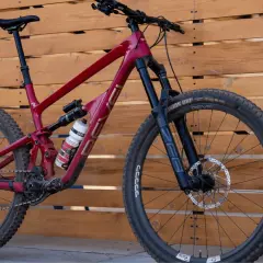A red Revel Rail mountain bike with a water bottle, parked against a wooden fence.