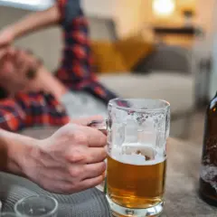 Mężczyzna leży na kanapie, trzymając kufel piwa. Wokół butelki piwa. Zastanawiasz się, ile % ma wódka?