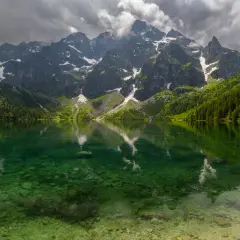 Morskie Oko z rowerem w tle, odbijające się w krystalicznie czystej wodzie. Majestatyczne góry i gęsty las tworzą malowniczy krajobraz.