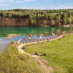 Turkusowe jezioro z drewnianą kładką i zielonymi terenami rekreacyjnymi.