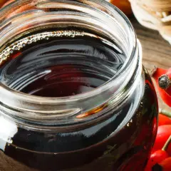 Słoik z ciemnym syropem z dzikiej róży, obok świeże owoce. Idealny przepis na domowy syrop z dzikiej róży.