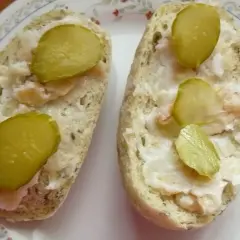 Dwa kawałki chleba z domowym smalcem po góralsku i plasterkami ogórka kiszonego.
