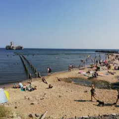 Słoneczna babie doły plaża tętni życiem. Ludzie opalają się, kąpią w morzu, a w oddali widać zabytkowy fort.