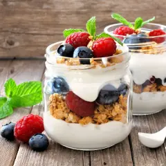 Dos frascos de vidrio con yogur, granola, frambuesas y arándanos. ¡Cuidado! El yogur con avena engorda si no se consume con moderación.